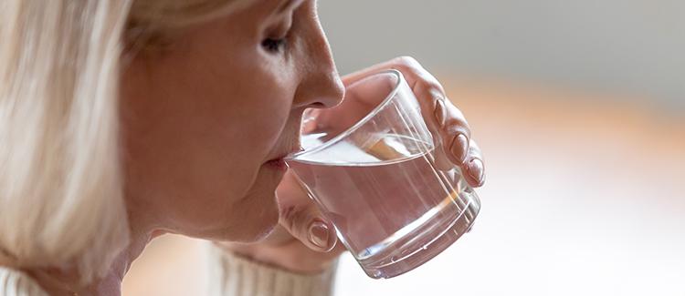 Ältere Frau trinkt Wasser aus einem Glas.