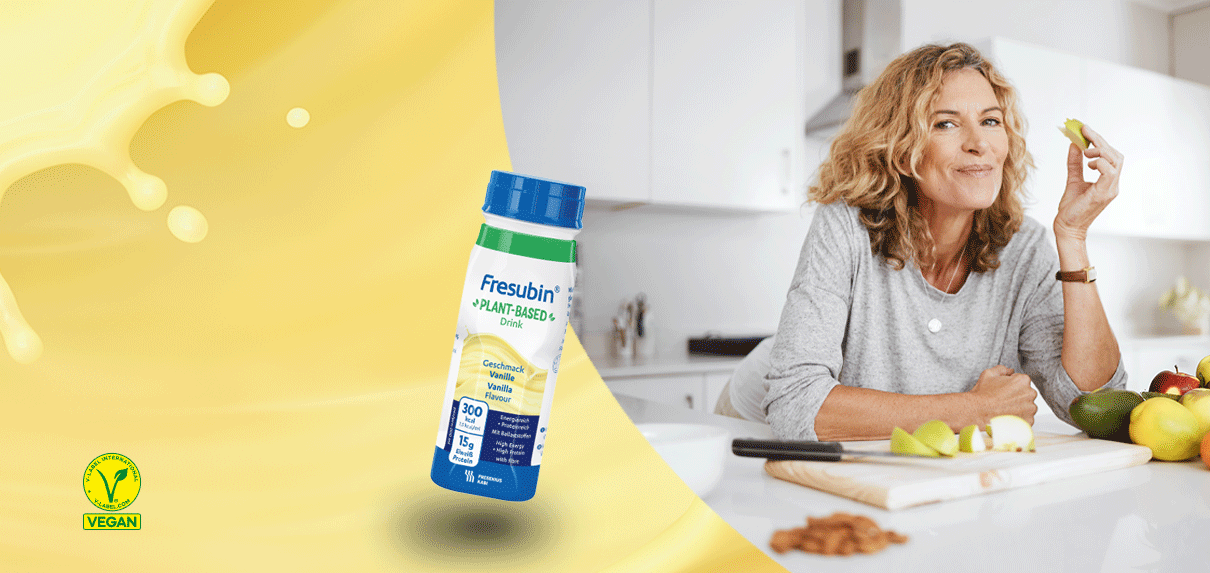Frau isst Obst in der Küche, daneben Fresubin Plant-Based Drink in Szene gesetzt.