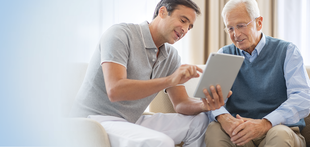 Junger Mann erklärt älterem Herrn Inhalte auf einem Tablet.