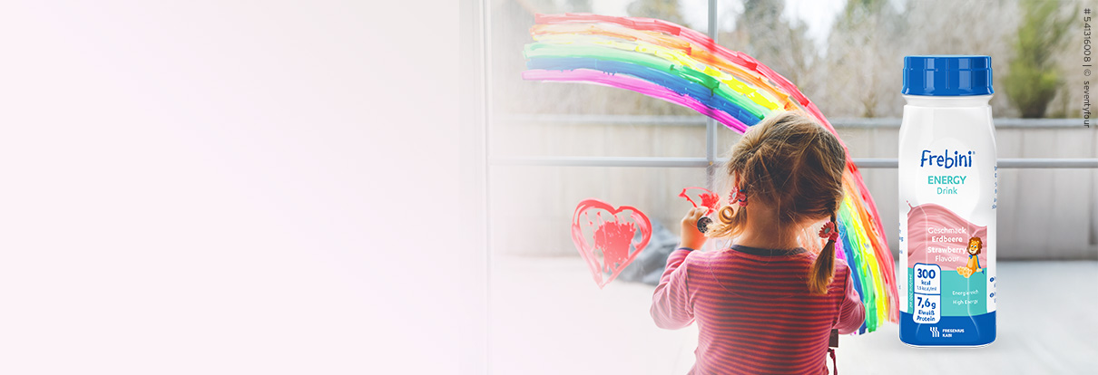Kleines Mädchen malt einen Regenbogen an die Fensterscheibe. Neben ihr ist die Frebini Trinknahrung.
