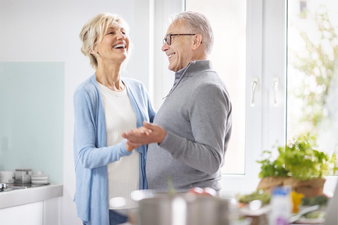 Patientin, die unter Mangelernährung leidet, tanzt mit ihrem Ehemann in der Küche während sie gemeinsam gesund kochen.