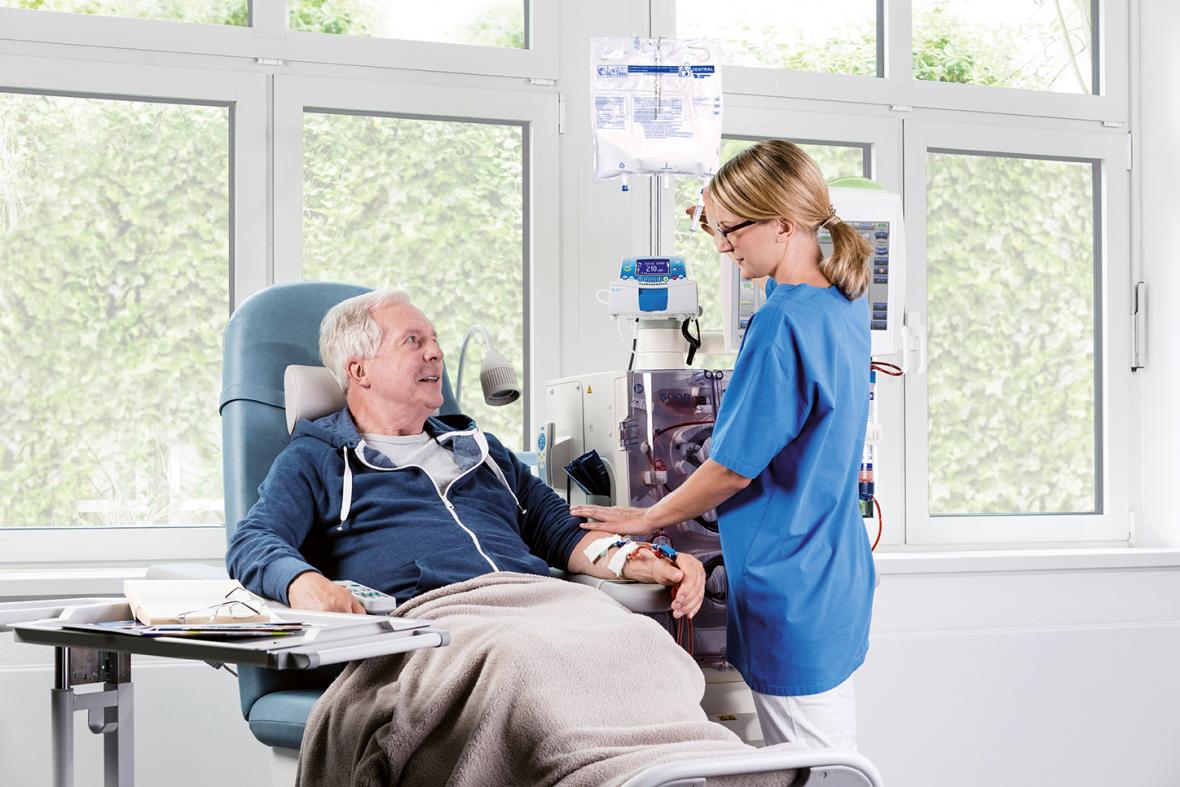 Patient während der Dialysebehandlung unterhält sich mit einer Pflegerin, die ihn an ein Dialysegerät anschließt - verlinkt zu Ernährung bei Dialyse