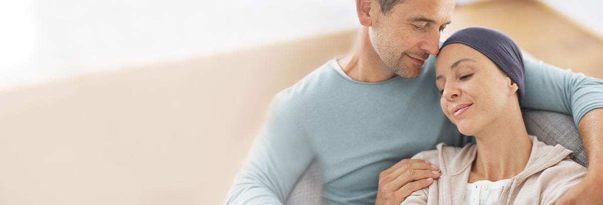 Krebspatientin liegt in den Armen ihres Mannes. Krebs und seine Therapie hintelassen Spuren, wobei eine ausgewogene Ernährung bei Gewichtsverlust helfen kann.