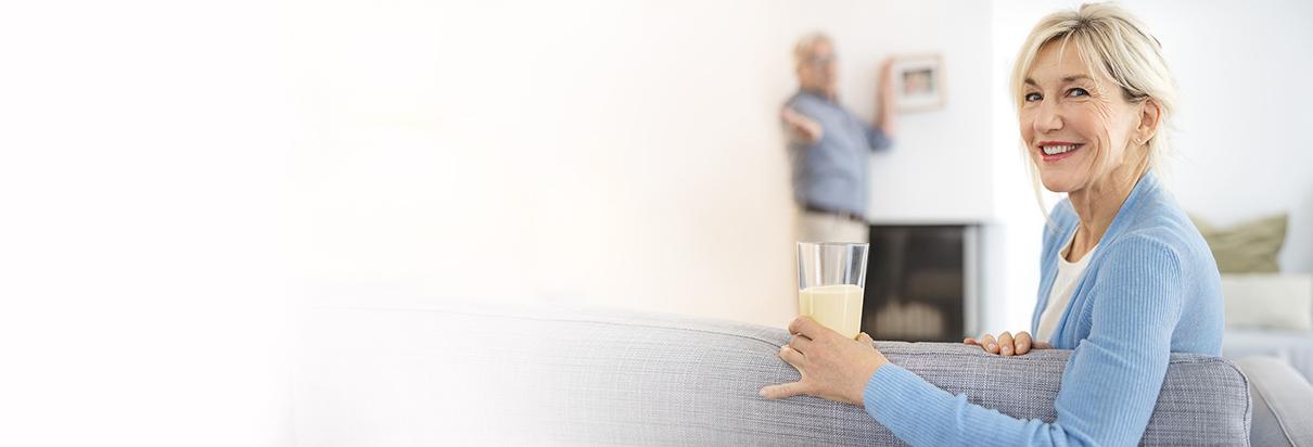 Ernährung bei Niereninsuffizienz: Patientin genießt ein großes Glas Fresubin auf ihrem Sofa