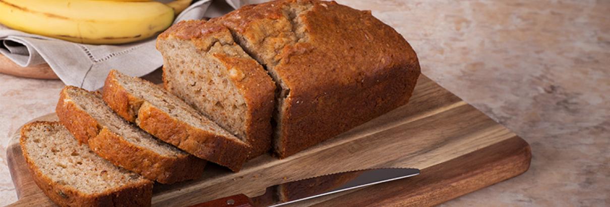 aufgeschnitten Veganes Bananen-Kürbis-Brot auf einem Holzbrett mit Bananen nebendran