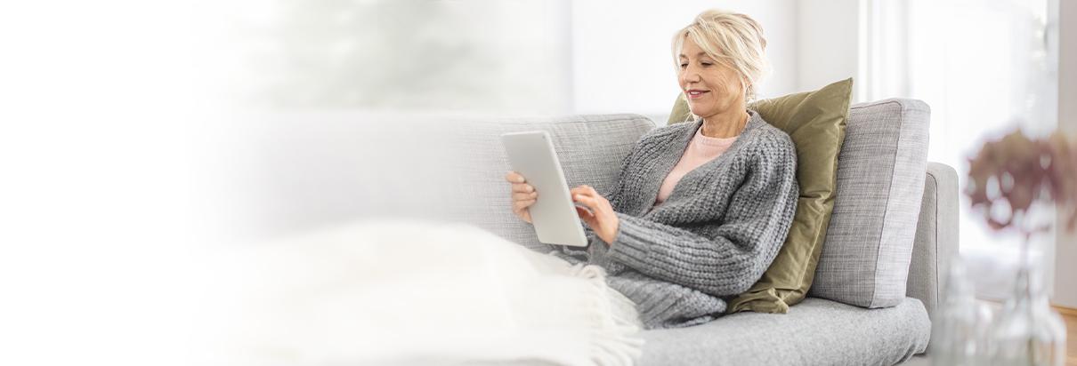 Eine ältere Frau liegt auf dem Sofa und surft online über ihr Tablet im Internet.